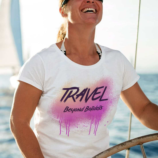 Ausgelassen lachende Frau am Ruder eines Seegelbootes. Weißes T-Shirt mit Print über einem Bikinioberteil.