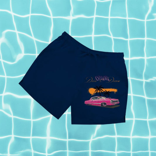Dunkelblaue Herren Badeshorts mit Aufdruck „Drive & Dream“ vor Poolwasser-Hintergrund.