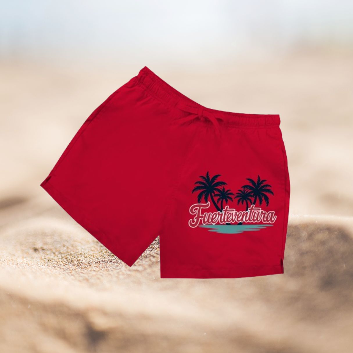 Rote Herren Badeshorts mit Palmenmotiv und Schriftzug Fuerteventura vor Sandhintergrund.