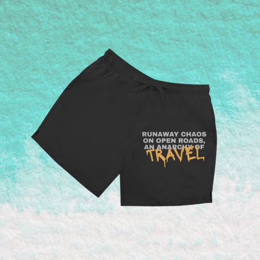 Schwarze Herren Badeshorts mit Schriftzug „RUNAWAY CHAOS“ vor türkisfarbenem Wasserhintergrund.