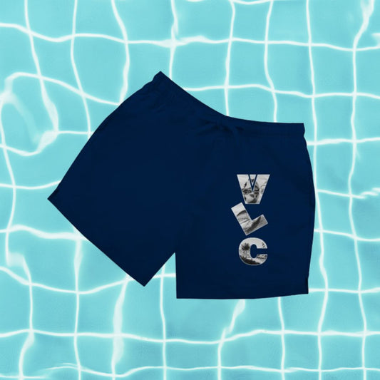 Dunkelblaue Herren Badeshorts mit Aufdruck „VLC“ (Airport-Code) vor Poolwasser-Hintergrund.