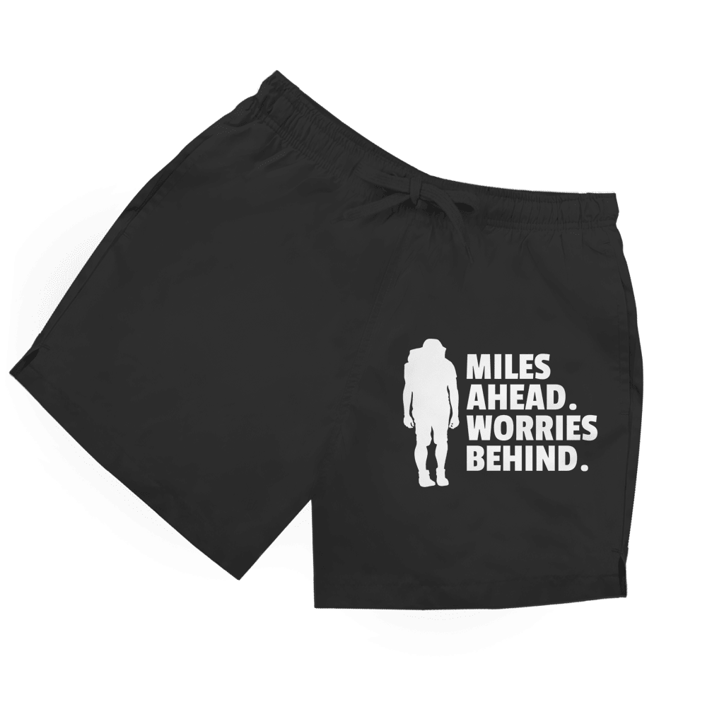 Schwarze Herren Badeshorts mit Wanderer-Silhouette und Schriftzug „Miles Ahead. Worries Behind.“ in weiss.