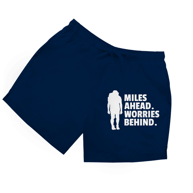 Dunkelblaue Herren Badeshorts mit Wanderer-Silhouette und Schriftzug „Miles Ahead. Worries Behind.“ in weiss.