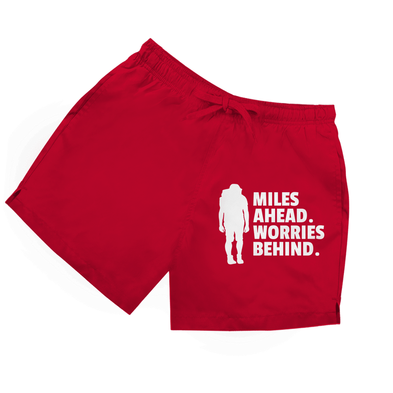Rote Herren Badeshorts mit Wanderer-Silhouette und Schriftzug „Miles Ahead. Worries Behind.“ in weiss.