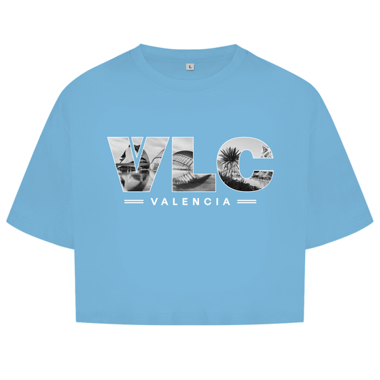 Hellblaues Oberteil mit dem Airport Code, horizontaler Druck. Als Overlay von VLC ein Bild mit Architektur und Palmen.