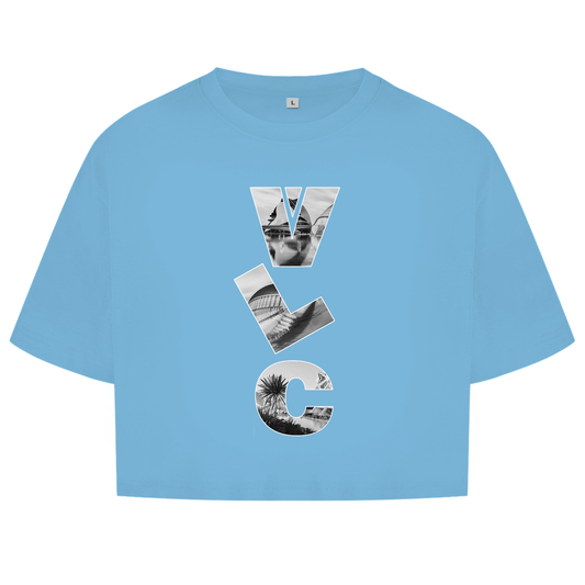 Hellblaues Oberteil mit dem Airport Code, vertikaler Druck. Als Overlay von VLC ein Bild mit Architektur und Palmen.