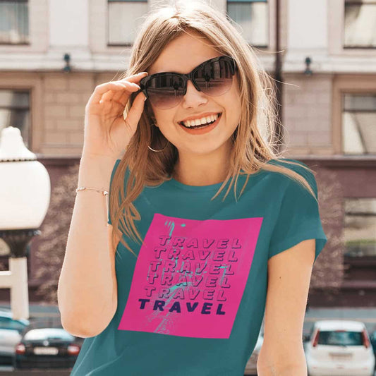 Junge Frau mit dunkelblondem Haar, Hand an der großen Sonnenrille. Sie trägt ein blaugrünes Shirt mit TRAVEL Print in pink.
