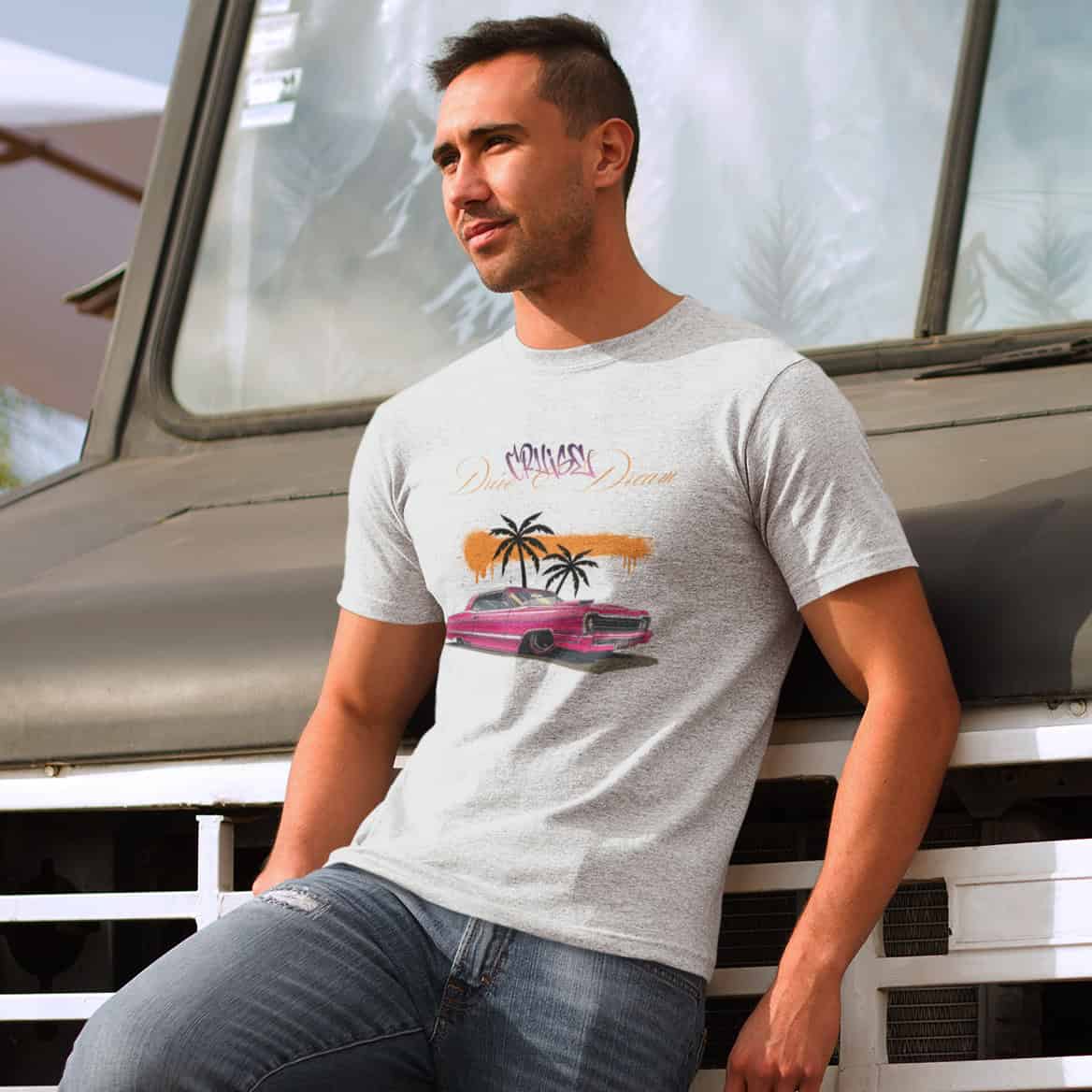Junger Mann lehnt lässig an einem Truck. Er trägt eine zerrissene Jeans und ein helles T-Shirt mit dem markanten Design.