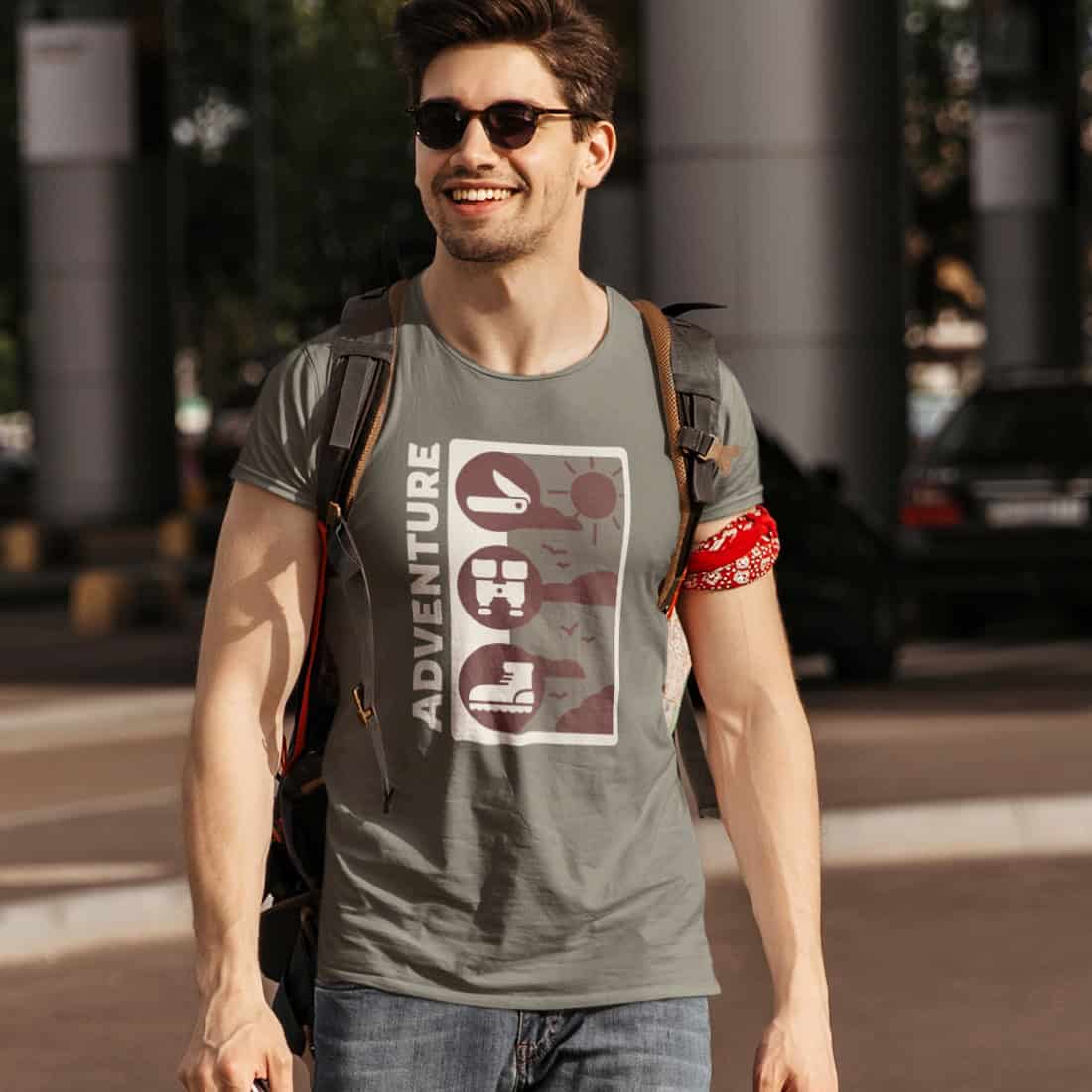 Sportlicher Typ in Jeans mit dunklem Haar, trägt Rucksack, Sonnenbrille und TShirt mit ADVENTURE-Design.