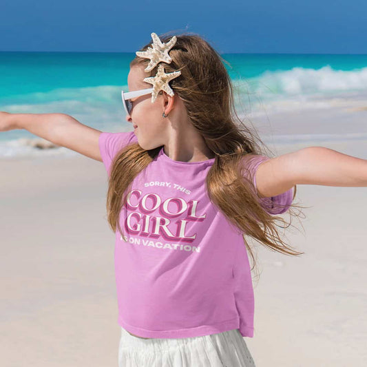 Türkisfarbes Wasser mit Wellen im Hintergrund. Am Strand ein Mädchen mit ausgebreiteten Armen und pinkfarbenes T-Shirt.