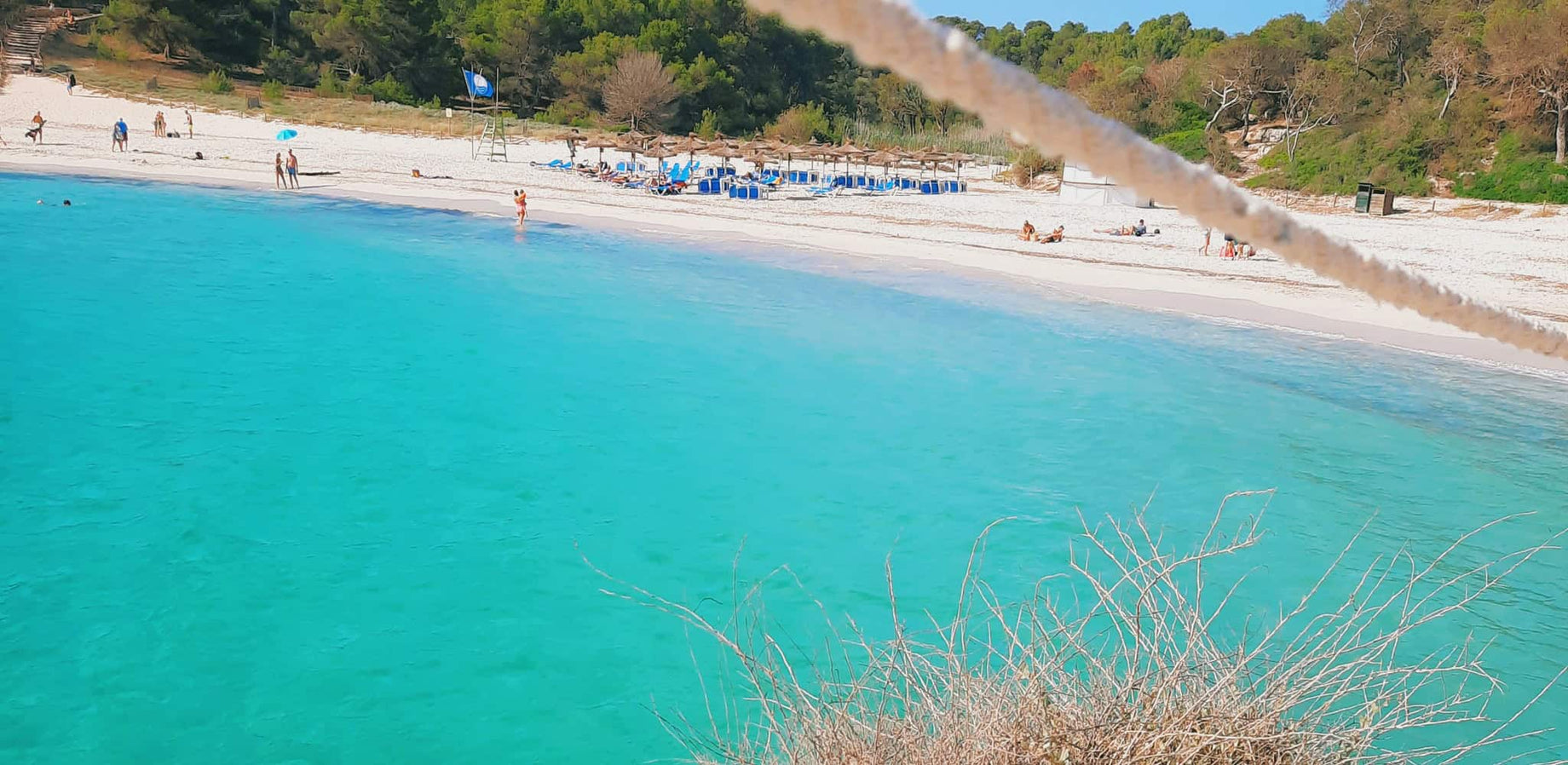Türkisfarbenes Wasser mit einem breiten Sandstrand mit einigen Leuten am und im Wasser (Playa de S'Amarador)